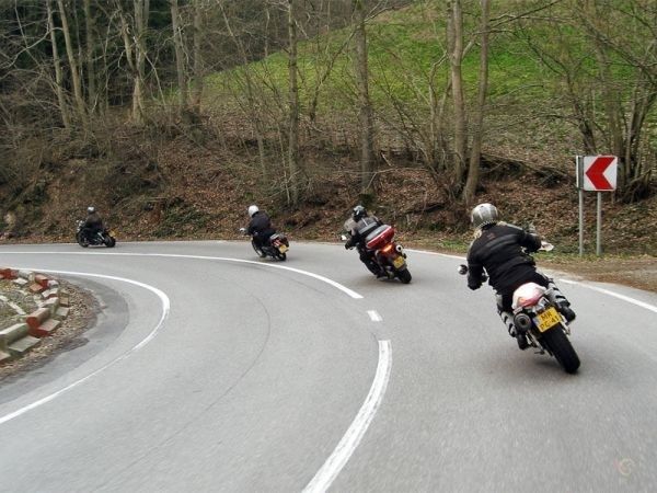 Four motorcyclists leaning through a sharply curved forest road