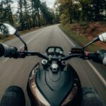 Motorcyclist gripping handlebars while riding through a forested curve