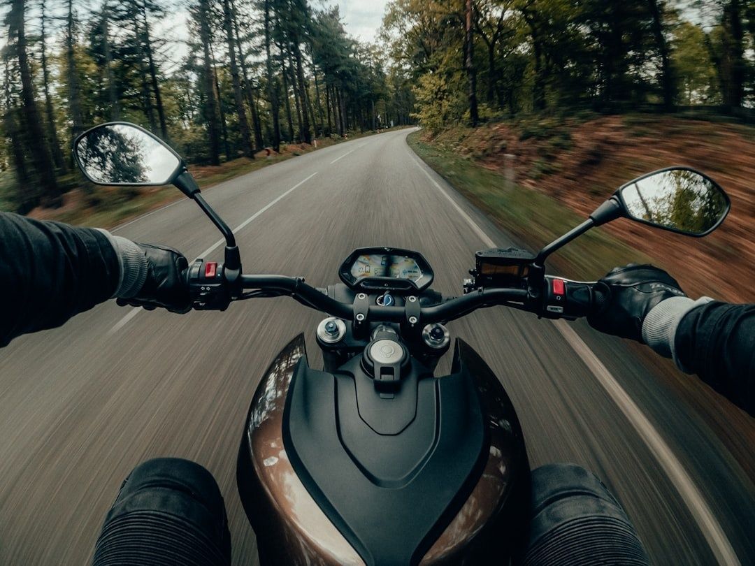 Motorcyclist gripping handlebars while riding through a forested curve